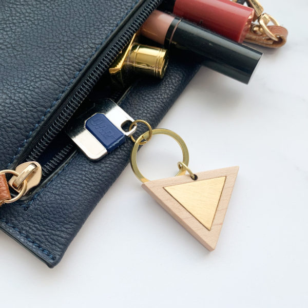 Pale white wood triangle key ring with brass metal inlay, displayed with key in purse