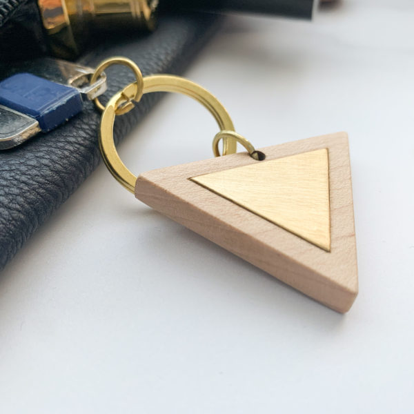 Pale white wood triangle key ring with brass metal inlay, displayed with key