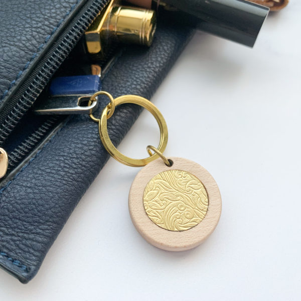 Pale white wood round key ring with brass inlay, displayed with key