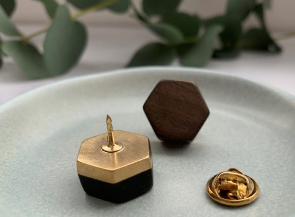 Brown wood and brass pin facing forward in background with black wood and brass pin in foreground face down, exposing pin