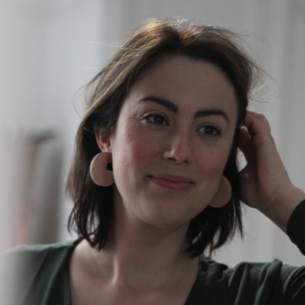 Model looks straight ahead, pushes hair behind ear, wearing maple wood, sector shaped, Vannucchi Jewellery, Ellie earrings