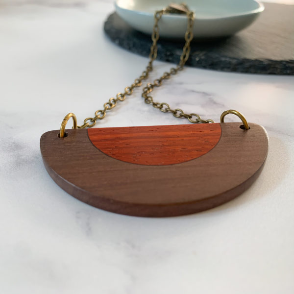 Belle brown and red wood semi circular necklace displayed draped over aqua coloured dish