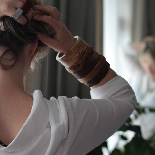 Model holds up hair and shows right arm full of wooden bangles