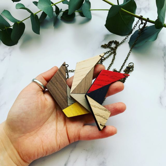 Models hand holding three colourful, geometric, wood necklaces