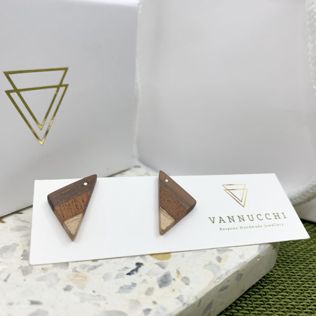 Triangular mixed wood earrings displayed in front of branded box