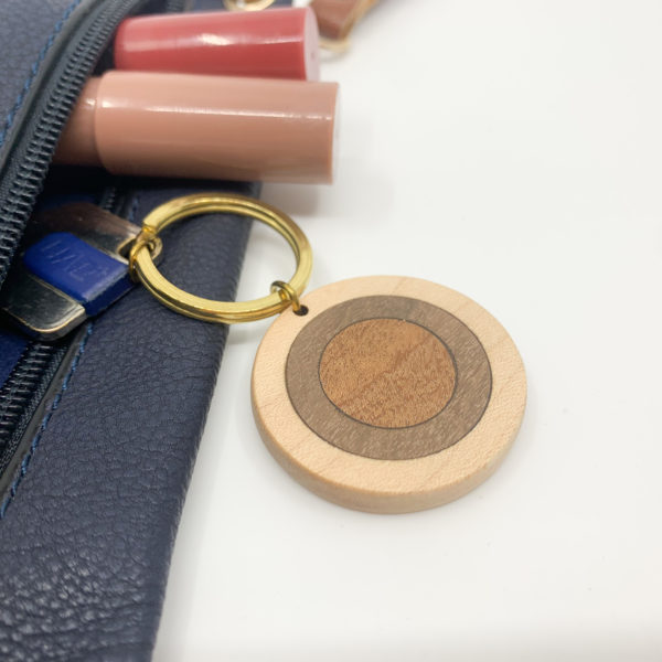 Round mixed wood key ring attached to key in pouch next to cosmetics