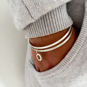 Model wears grey jumper, hand in pocket, wearing a collezione xxi pebble bangle with a second silver bangle.