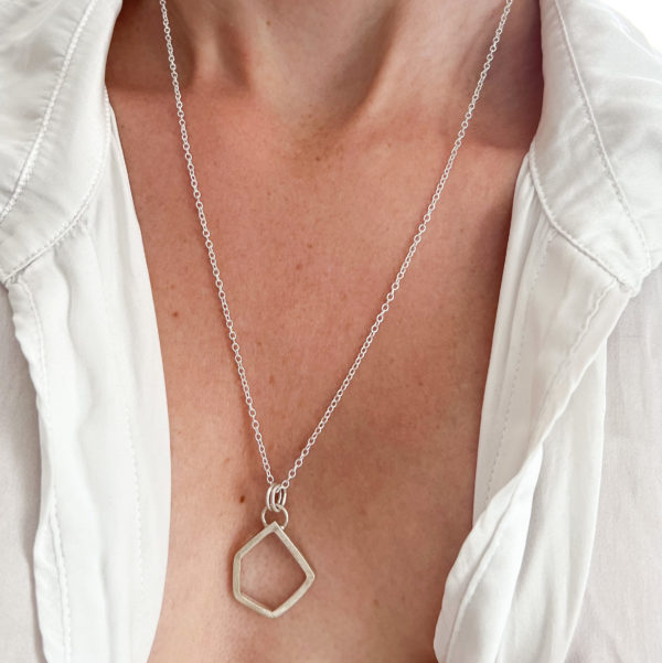 Model wears white shirt, slightly open to expose the Collezione XXI Large Stone Necklace. Long fine Silver Chain holds a silver, square wire, irregular geometric pendant.