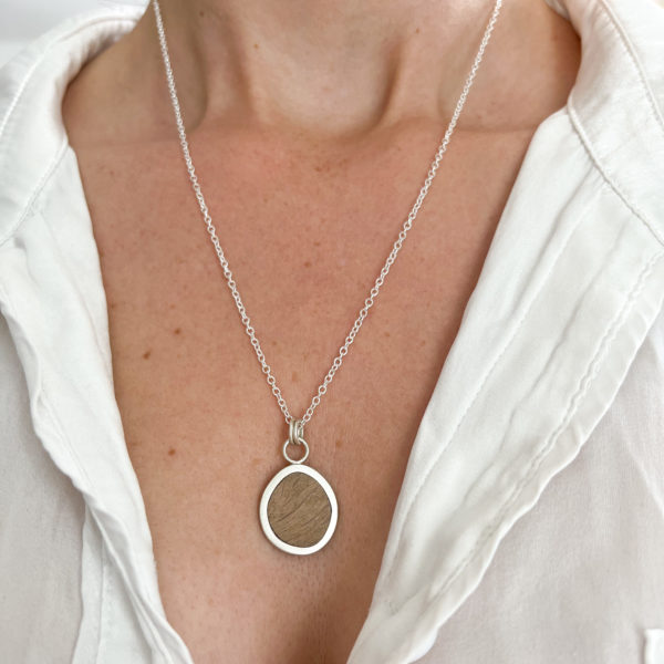 Model wears white shirt partially open to show Collezione XXI Oak Pebble Necklace. Long fine silver chain, with silver and oak pebble shaped pendant