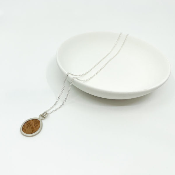 Collezione XXI Oak Pebble Necklace displayed on white background. Laid over a white dish. Long fine silver chain with silver and oak pendant.