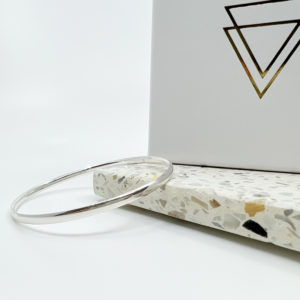 The Collezione XXI Bangle is a thin, high polished bangle, laid over a pale terrazzo tile in a white background with white Vannucchi packaging behind.