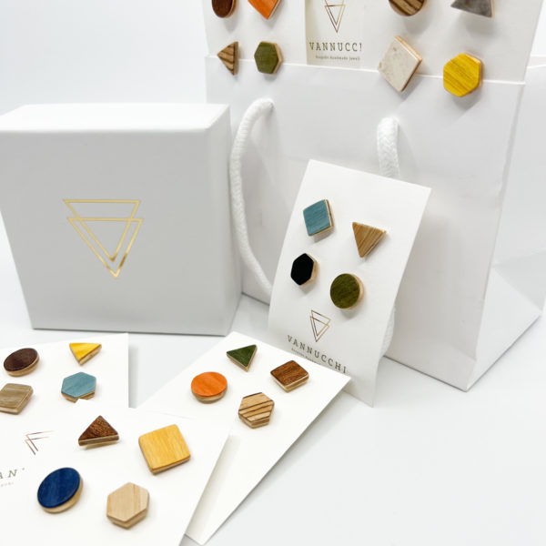 A side shot of a selection of mix and match veneer pin sets. Sets are of four geometric shaped ply wood pins. Displayed with white Vannucchi packaging on a white background.