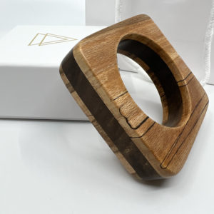 Marta mixed wood square bangle displayed at an angle with branded box on white background