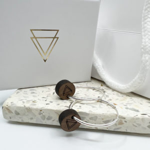 Vannucchi icon on walnut round charm on silver hoop earring. Displayed on pale terrazzo tile with branded box in background