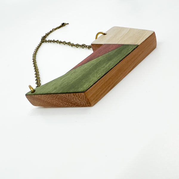 Vannucchi Origini Geometric Necklace at a low sideways view. Can see all the different coloured woods used. Pale pink red grandis wood base, green, red and white geometric shape marquetry top.
