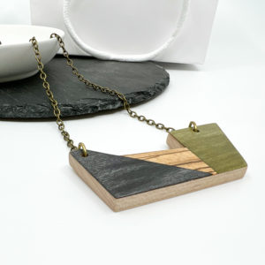 Verde geometric necklace on white background, displayed with plain white dish laid over dark grey slate.