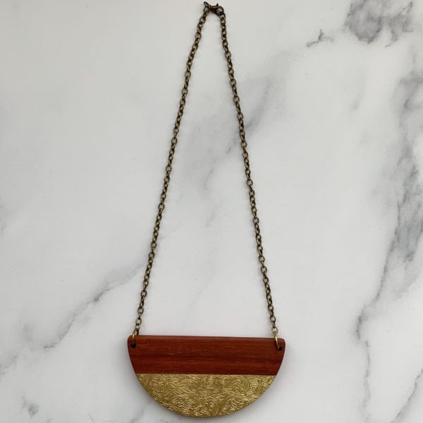 Aerial view of padauk and floral brass necklace at full length on marbled background.