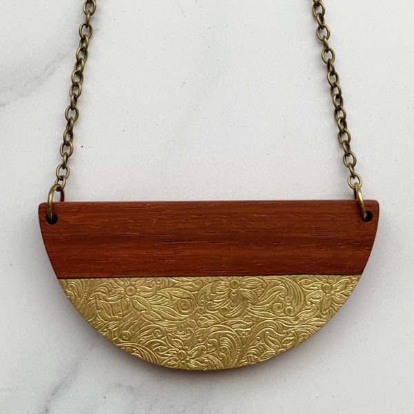 Close up of vibrant red wood padauk with floral brass inlay necklace. Semi circular.