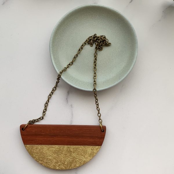 Padauk and floral brass inlay necklace displayed on marbled background laid over a small teal dish.